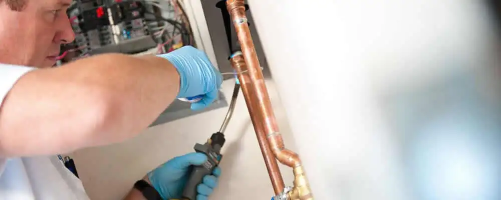 Water heater repair technician testing copper pipe connections and controls in Charlotte, NC